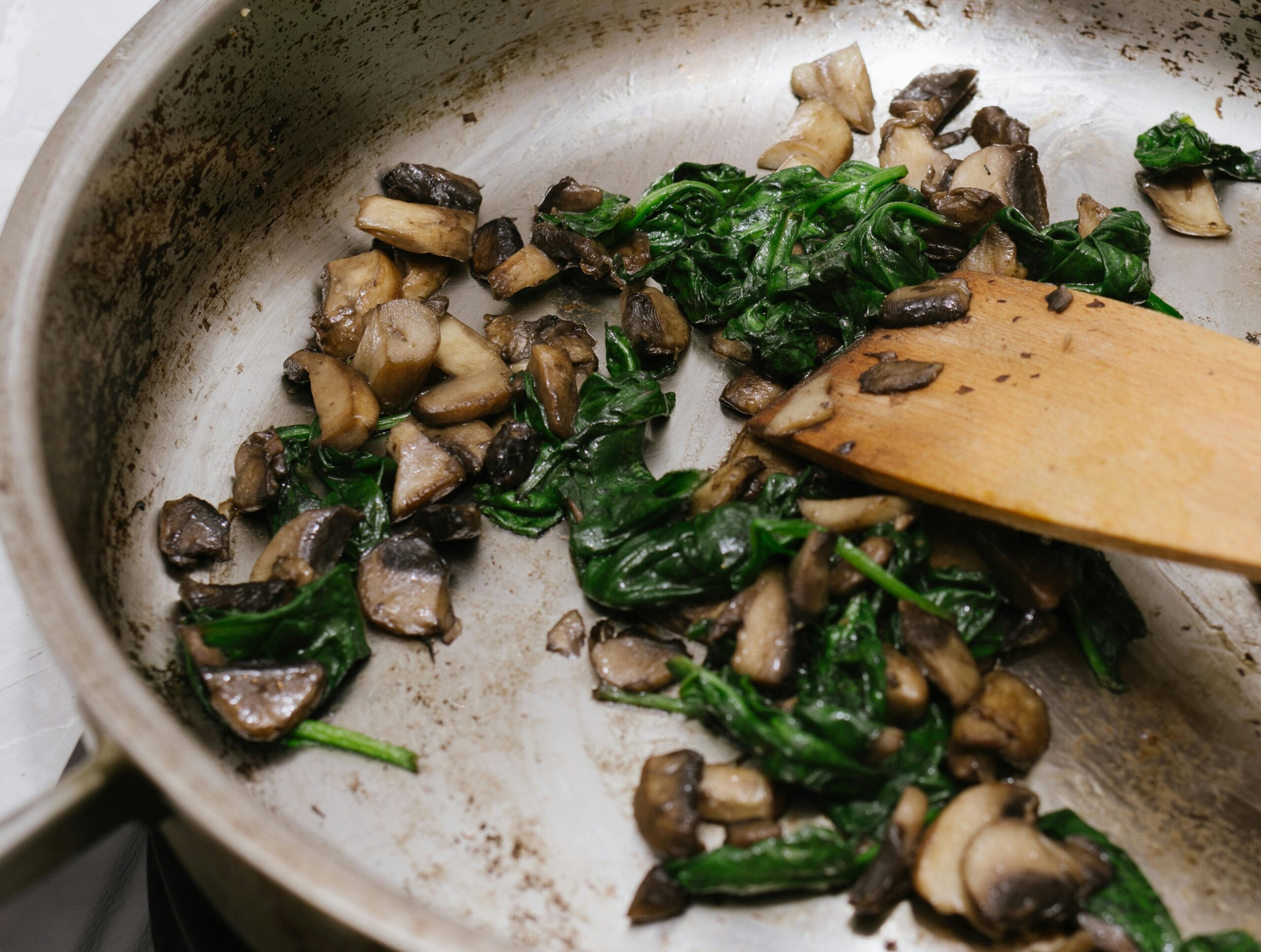 Sautéed spinach and mushrooms in a skillet with a wooden spatula captured mid-cook.